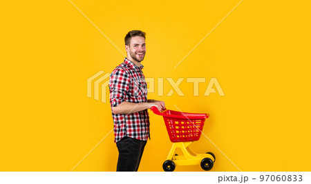 man go shopping. funny man with small shopping cart. weekend on buying products. rejoices successful purchases. spends money unwisely. customer pushing cart. buyer in supermarket. empty toy trolley 97060833