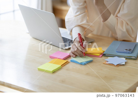 付箋にメモをする若い女性の手元 97063143