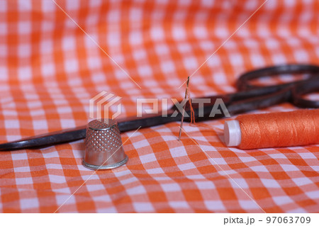 Orange and White Checkered Fabric With Thimble and Spool of Orange Thread Orange and White Checkered Fabric With Thimble and Spool of Orange Thread 97063709