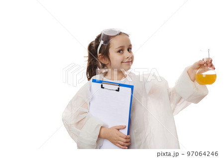 Smart elementary school student, adorable little girl, young chemist-scientist in lab coat, holding flask with yellow liquid chemical substance and clipboard with blank sheets, on white background 97064246