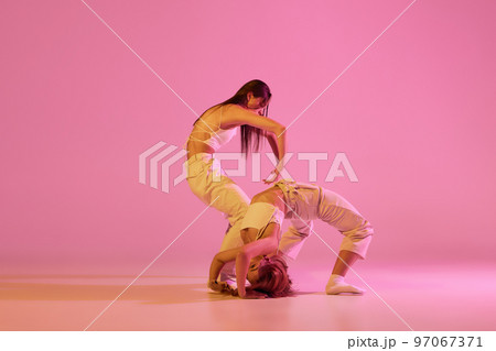 Modern dance art. Young girls, couple of dancers in sports style clothes dancing experimental dances isolated over light pink background in neon. Concept of music, emotions, dance 97067371