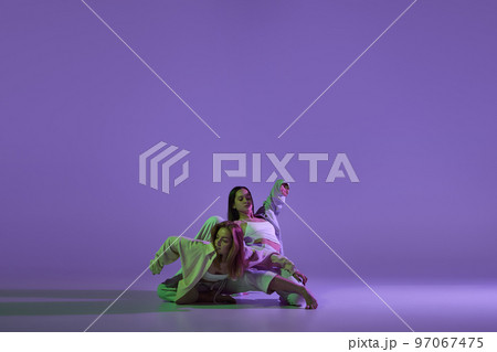 Dance performance. Stylish female dancers at contemporary choreography dance class isolated over crystal purple background. Style, youth, music and fashion 97067475