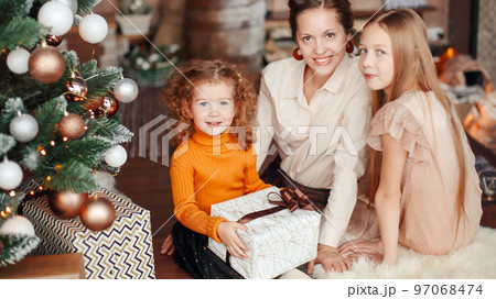mother and her daughters opening a gift box near the Christmas t 97068474