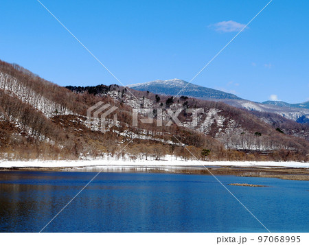 早春の裏磐梯、秋元湖。湖面の雪原は消え、真っ青な湖水が現れ、岸辺の白い残雪とのコントラストが綺麗 97068995