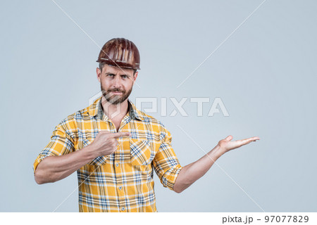 handsome man foreman in helmet and checkered shirt presenting product, copy space, advertisement. handsome man foreman in helmet and checkered shirt presenting product, copy space, advertisement. 97077829