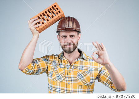 labor or workers day. man laborer with brick. guy wear worker uniform. handsome builder in helmet labor or workers day. man laborer with brick. guy wear worker uniform. handsome builder in helmet 97077830