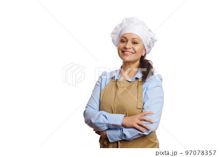 Cheerful female baker confectioner, pastry chef, female cook, waitress in chef's hat and apron, smiling a cheerful toothy smile looking at camera, isolated on white background. Copy advertising space Cheerful female baker confectioner, pastry chef, female cook, waitress in chef's hat and apron, smiling a cheerful toothy smile looking at camera, isolated on white background. Copy advertising space 97078357