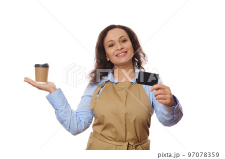 Isolated portrait on white background of a pretty woman in casual blue shirt and beige chef apron, holding a takeaway drink in paper cup and showing on camera a credit card with copy advertising space Isolated portrait on white background of a pretty woman in casual blue shirt and beige chef apron, holding a takeaway drink in paper cup and showing on camera a credit card with copy advertising space 97078359