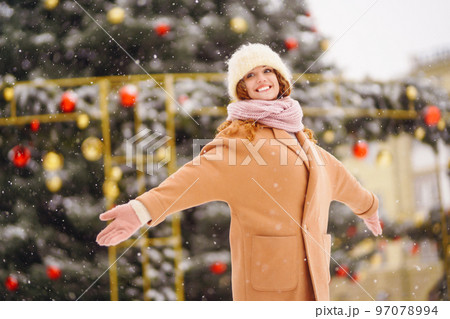 Young woman in winter style clothes posing at festive street market. Cold weather. Winter fashion. 97078994