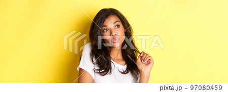 Image of silly and cute african-american girl, pouting and looking left, standing over yellow background Image of silly and cute african-american girl, pouting and looking left, standing over yellow background 97080459
