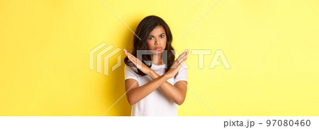 Image of disappointed and angry african-american woman, telling no, showing stop sign and frowning, prohibit and disagree with you, standing over yellow background Image of disappointed and angry african-american woman, telling no, showing stop sign and frowning, prohibit and disagree with you, standing over yellow background 97080460