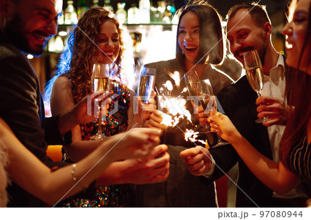 Glowing sparkles in hands. Group of happy people enjoying party with fireworks. Winter holiday. 97080944