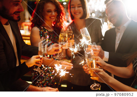 Glowing sparkles in hands. Group of happy people enjoying party with fireworks. Winter holiday. 97080952