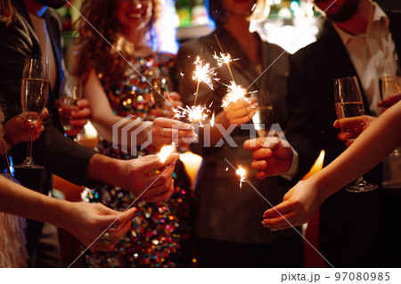 Glowing sparkles in hands. Group of happy people enjoying party with fireworks. Winter holiday. 97080985