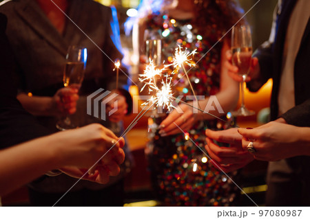 Glowing sparkles in hands. Group of happy people enjoying party with fireworks. Winter holiday. 97080987