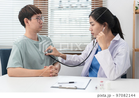 Female doctor physician is examines heart and lungs of male patient with a stethoscope to check Female doctor physician is examines heart and lungs of male patient with a stethoscope to check 97082144