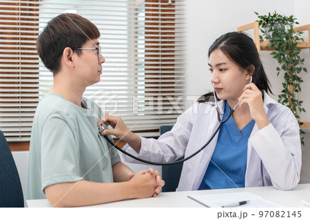 Female doctor physician is examines heart and lungs of male patient with a stethoscope to check Female doctor physician is examines heart and lungs of male patient with a stethoscope to check 97082145