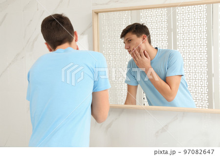 Teen guy with acne problem near mirror in bathroom 97082647