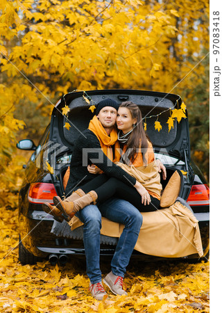 A happy couple sits on the trunk of a car, enjoying the view of autumn. The concept of travel and weekend holidays. 97083418