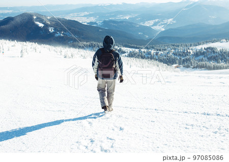Man with backpack trekking in mountains. Cold weather, snow on hills. Winter hiking. 97085086
