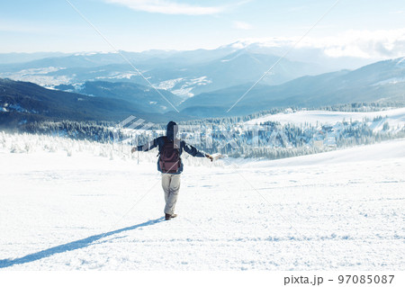 Man with backpack trekking in mountains. Cold weather, snow on hills. Winter hiking. 97085087