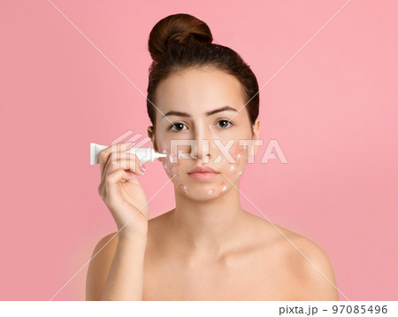 Teen girl with acne problem applying cream on light pink background Teen girl with acne problem applying cream on light pink background 97085496