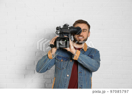 Operator with professional video camera near white brick wall 97085797