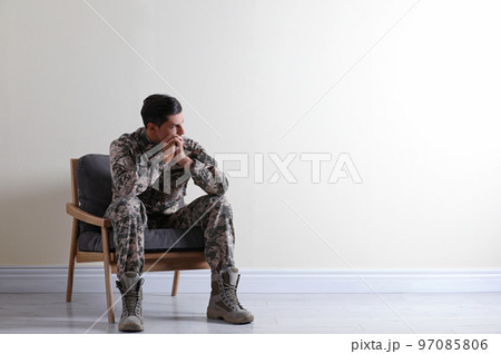 Stressed military officer sitting in armchair near white wall indoors. Space for text 97085806