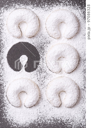 Heavy dusted vanilla crescents, with one missing on a baking tray. Vanillekipferl, crescent shaped Christmas biscuits, originally from Austria made with walnuts, butter, flour and vanilla icing sugar. 97086328