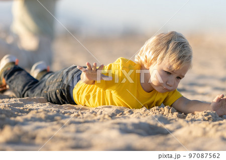 Blond little boy lying on the sand Blond little boy lying on the sand 97087562