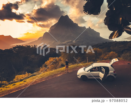 Car travel concept. People watching sunset over mountain peak on tropical Moorea island, Polynesia. Majestic sunset of the mountains landscape. Stunning wild nature during sunrise. Vintage retro tone. Car travel concept. People watching sunset over mountain peak on tropical Moorea island, Polynesia. Majestic sunset of the mountains landscape. Stunning wild nature during sunrise. Vintage retro tone. 97088052