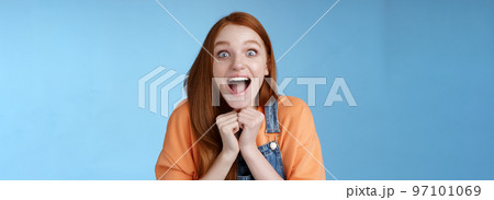 Cute redhead european girl blue eyes freckles reacting amused shocking rumor lift eyebrows drop jaw surprised smiling excited picked get role theatre play rejoicing astonished blue background 97101069