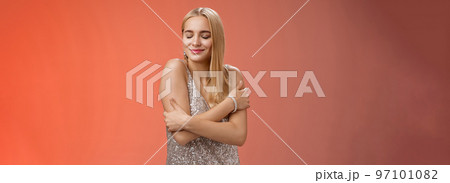 Tender feminine elegant blond young woman in stylish silver glittering dress close eyes dreamy smiling touching herself cuddle embrace hands crossed body remember heartwarming passionate feelings Tender feminine elegant blond young woman in stylish silver glittering dress close eyes dreamy smiling touching herself cuddle embrace hands crossed body remember heartwarming passionate feelings 97101082