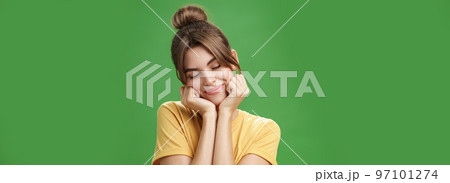 Tender sensual timid european girl in yellow t-shirt leaning head on shoulder touching cheeks with hands closing eyes and smiling with soft grin feeling nostalgic and romantic over green background Tender sensual timid european girl in yellow t-shirt leaning head on shoulder touching cheeks with hands closing eyes and smiling with soft grin feeling nostalgic and romantic over green background 97101274