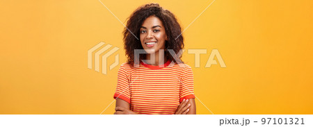 Waist-up shot of creative ambitious good-looking female coworker in trendy striped t-shirt holding hands crossed on chest smiling broadly at camera friendly and self-assured over orange background Waist-up shot of creative ambitious good-looking female coworker in trendy striped t-shirt holding hands crossed on chest smiling broadly at camera friendly and self-assured over orange background 97101321