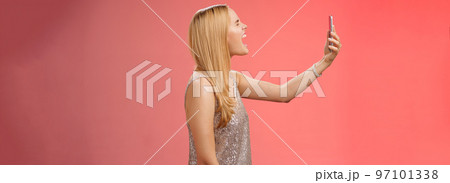 Profile shot funny carefree blond woman hold smartphone raised open mouth wide yelling recording video own shout scream, standing silver glamour dress near red background fool around Profile shot funny carefree blond woman hold smartphone raised open mouth wide yelling recording video own shout scream, standing silver glamour dress near red background fool around 97101338