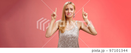 Upset whining immature spoiled blond rich girl in silver glittering dress pouting frowning gonna cry pointing up regret jealousy begging buy expensive shoes, standing red background displeased Upset whining immature spoiled blond rich girl in silver glittering dress pouting frowning gonna cry pointing up regret jealousy begging buy expensive shoes, standing red background displeased 97101344