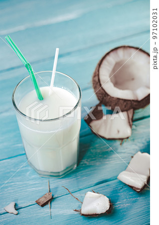 Top view of coconut milk in glass with coconut on white wooden table. Selective focus. Tropical 97102031