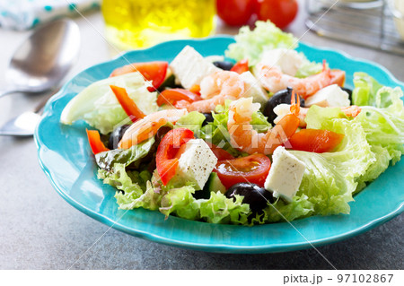 The concept of healthy and dietary food. Healthy salad close-up, Greek salad with shrimps and vegetables on a light stone or slate table. 97102867