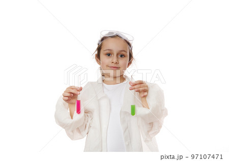 Lovely child girl, future chemist scientist in lab coat, smiles looking at camera, holding out test tubes with liquid chemical, isolated on white background. Kids learning chemistry. Education concept Lovely child girl, future chemist scientist in lab coat, smiles looking at camera, holding out test tubes with liquid chemical, isolated on white background. Kids learning chemistry. Education concept 97107471