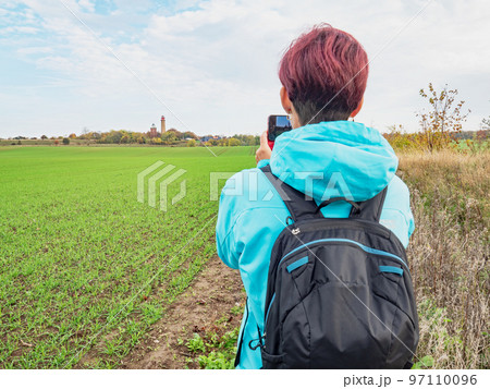 Woman takes travel photos of field and  lighthouse Kap Arkona. 97110096