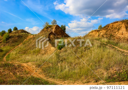 Hilly sandy terrain, part of a motocross track against a blue sky 97111121