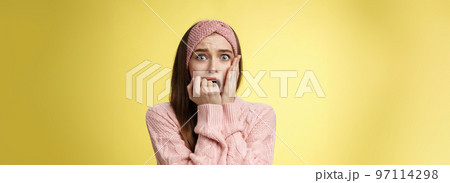 Shocked frightened stunned cute timid girl panicking, standing in stupor biting fist in fear staring terrified pressing palm to chest worried, upset, innocent woman become witness of crime stupefied 97114298