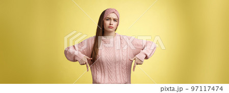 Why me, gosh. Gloomy upset complaining cute glamout young european girl in casual sweater, headband frowning, whining grimacing displeased pointing down, unhappy see lots work over yellow wall 97117474