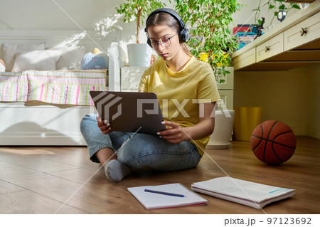 Teenage girl with headphones studying at home using a laptop Teenage girl with headphones studying at home using a laptop 97123692