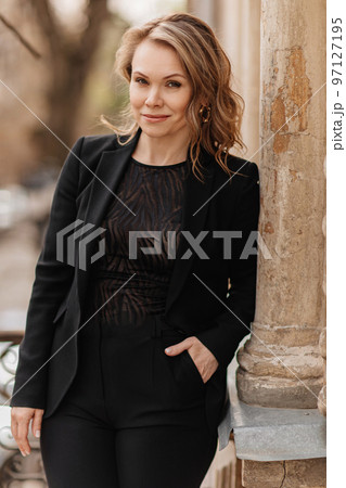 a beautiful, confident woman in a black suit on the balcony of the old building. a beautiful, confident woman in a black suit on the balcony of the old building. 97127195