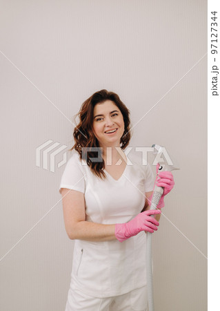 Portrait of the master of laser hair removal. A woman in a white coat holds a laser hair removal device in her hands 97127344