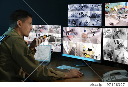 Security guard with portable transmitter monitoring modern CCTV cameras indoors 97128397