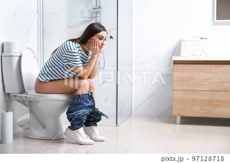 Upset woman sitting on toilet bowl in bathroom 97128718