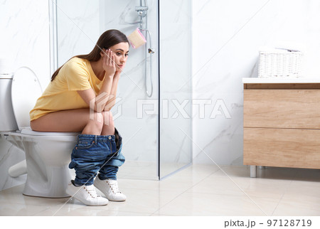 Upset woman sitting on toilet bowl in bathroom 97128719